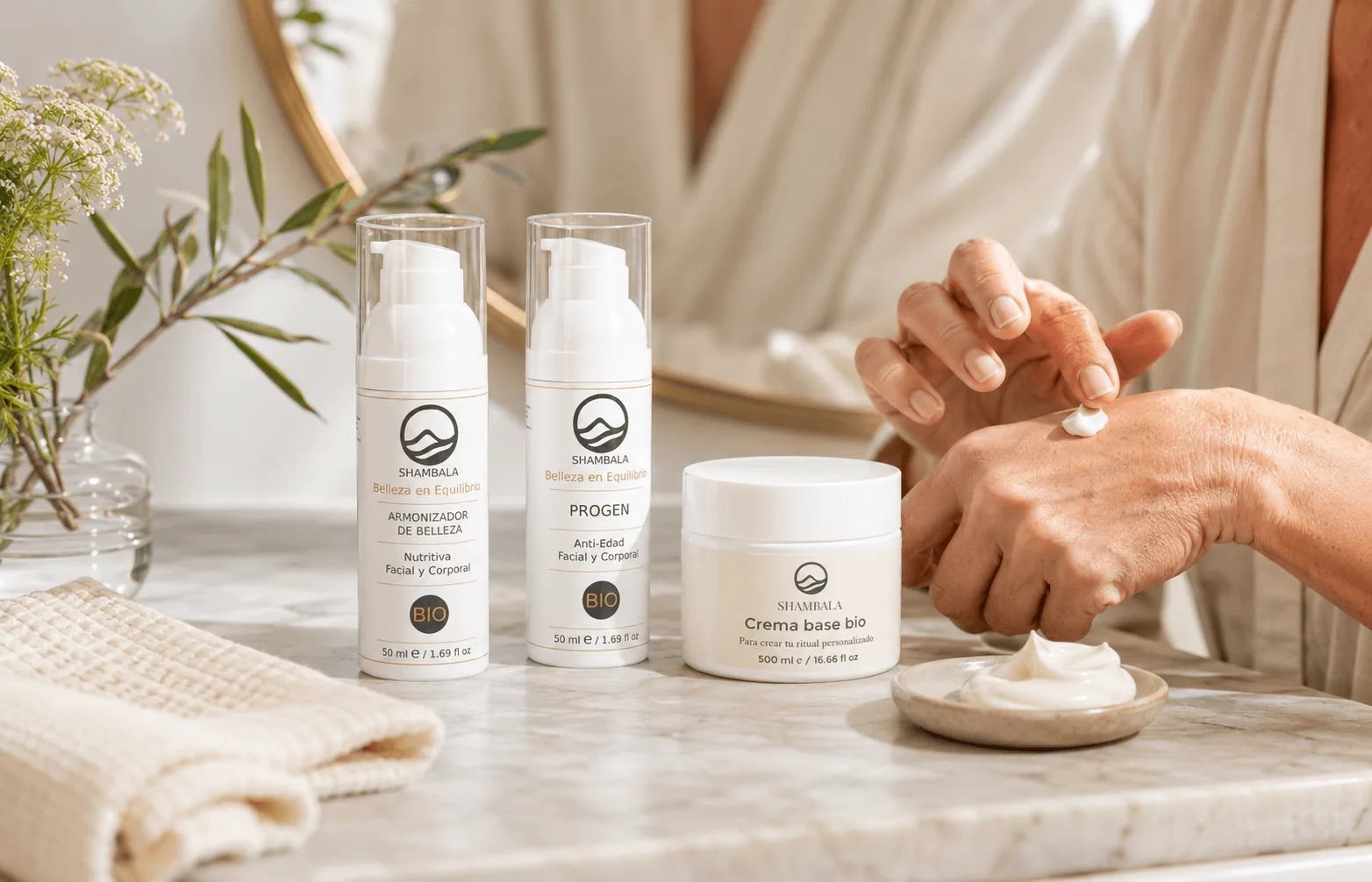 Armonizador de Belleza, Progen y Crema Base Bio Shambala en encimera de mármol con mano aplicando crema
